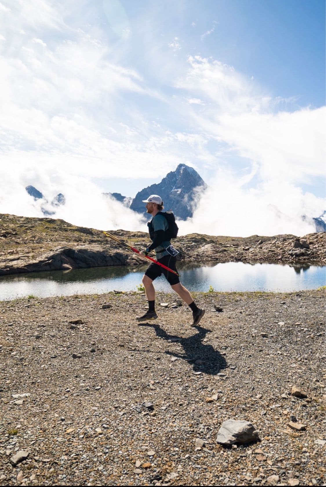 En trail, bâtons à la main, devant un lac d’altitude